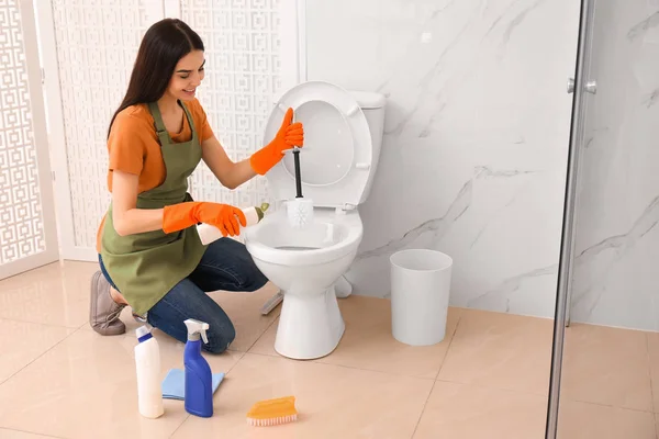 Молодая женщина чистит унитаз в ванной комнате — стоковое фото