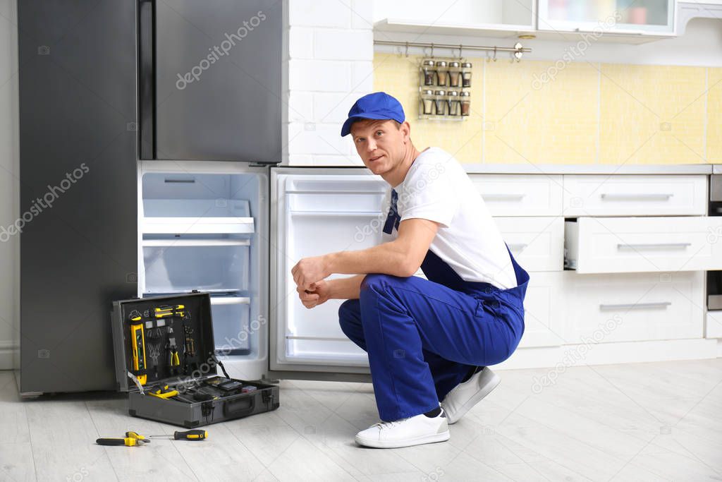 Male technician repairing broken refrigerator in kitchen