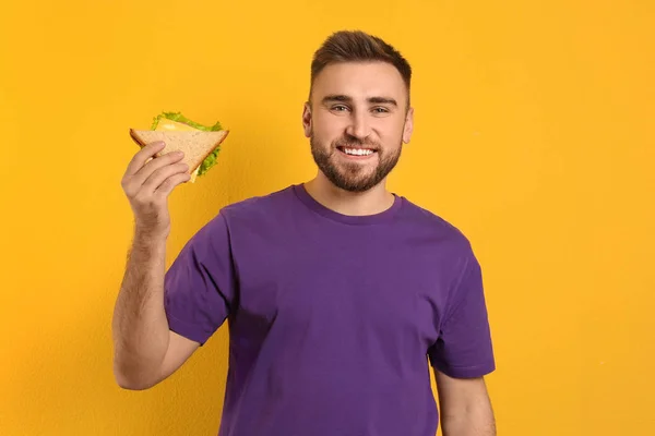 Young man with tasty sandwich on yellow background — Stock Photo, Image
