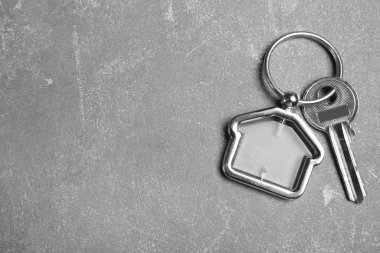 Gri taş zemin üzerinde ev şeklinde incik boncuklu anahtar, üst görünüm ve metin için boşluk. Emlakçılık hizmetleri