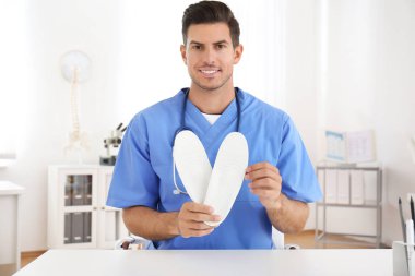 Handsome male orthopedist showing insoles in clinic clipart