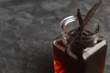 Aromatik ev yapımı vanilya özü ve gri masadaki kuru kapsüller, yakın plan. Metin için boşluk