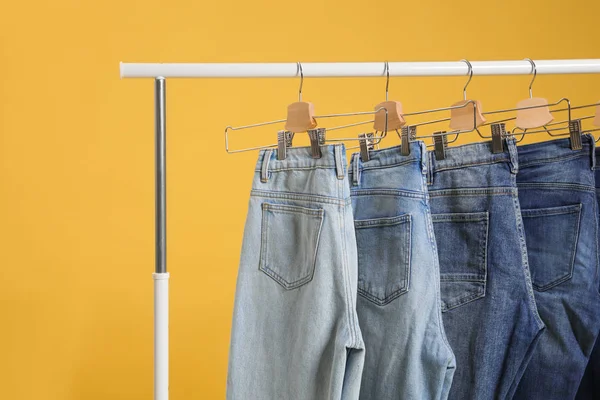 Rack with different jeans on yellow background — Stock Photo, Image