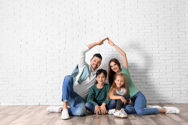 Família feliz formando telhado com as mãos perto da parede de tijolo. Insu — Fotografia de Stock