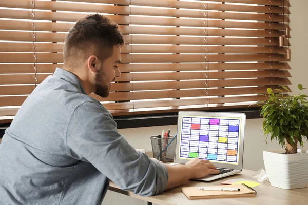 Genç adam ofisteki dizüstü bilgisayarında takvim uygulaması kullanıyor. — Stok fotoğraf