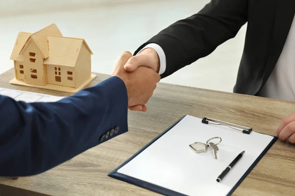 Immobilienmakler schüttelt Klientin am Tisch im Büro die Hand, — Stockfoto