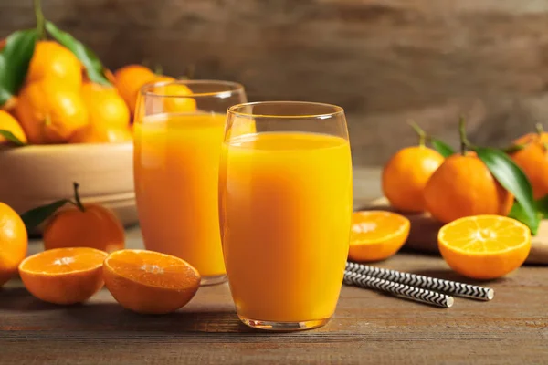 Szklanki świeżego soku mandarynkowego i owoców na drewnianym stole — Zdjęcie stockowe