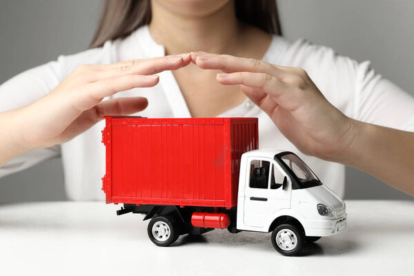 Woman covering toy truck at white table, closeup. Logistics and wholesale concept