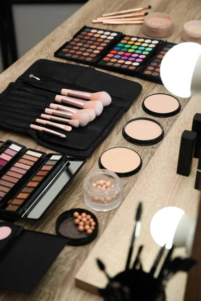 Set of different professional makeup products on wooden table in studio