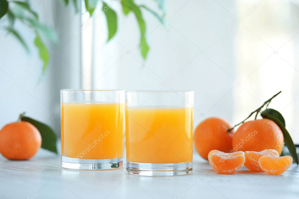 Glasses of fresh tangerine juice and fruits on white wooden tabl