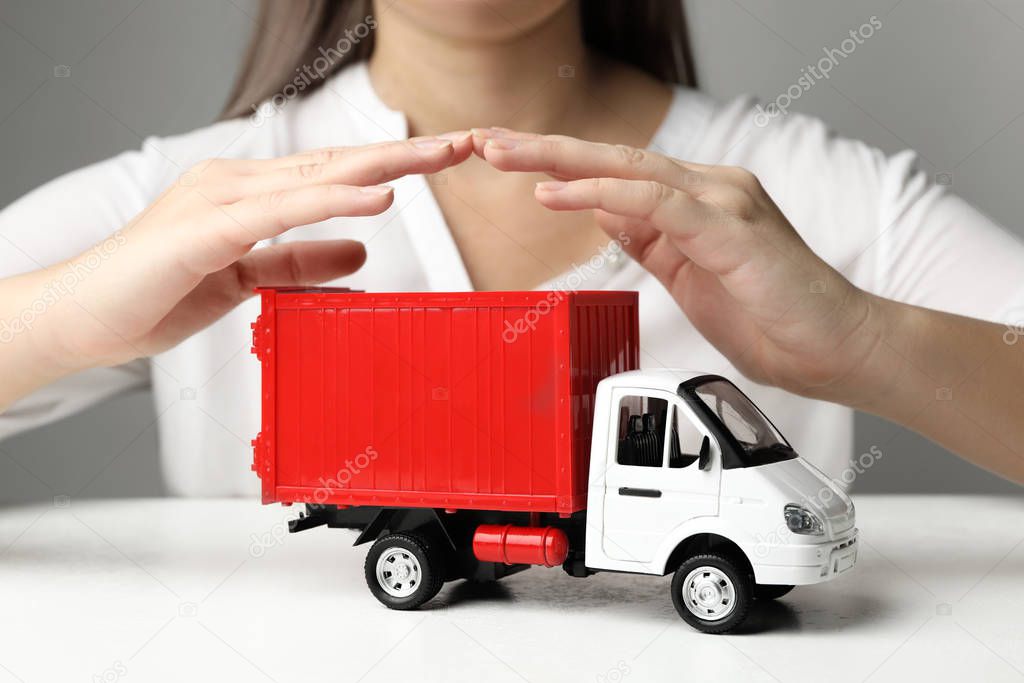 Woman covering toy truck at white table, closeup. Logistics and wholesale concept