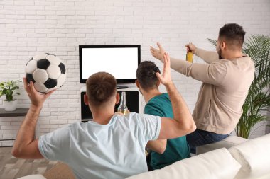 Bir grup arkadaş evde, arka planda futbol izliyorlar.