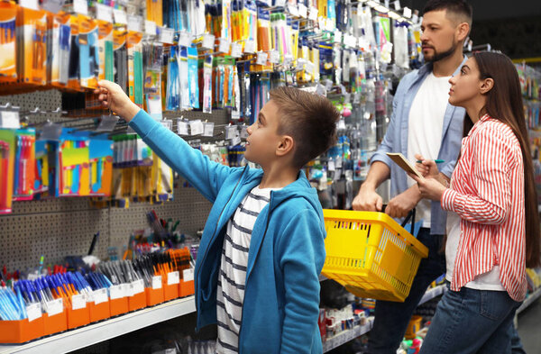 Family with little boy choosing school stationery in supermarket