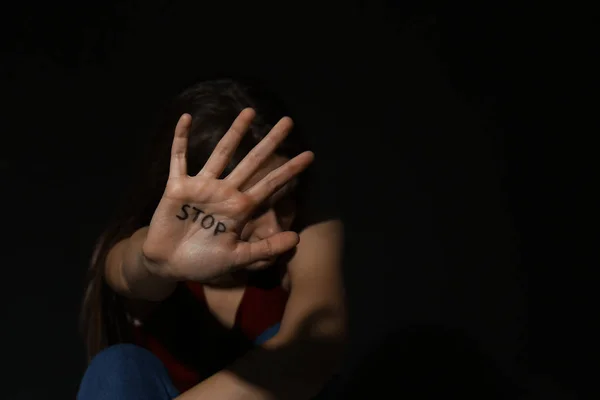 Mujer joven maltratada mostrando la palma de la mano con la palabra STOP contra negro bac —  Fotos de Stock