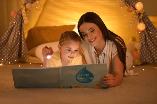 Mãe e filha com lanterna livro de leitura em casa — Fotografia de Stock