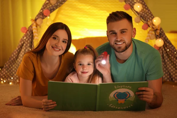 Família com lanterna livro de leitura em casa — Fotografia de Stock