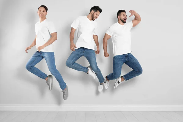 Grupo de hombres jóvenes en jeans elegantes saltando cerca de la pared de luz — Foto de Stock