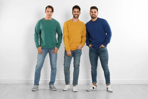 Grupp av unga män i snygga jeans nära vit vägg — Stockfoto