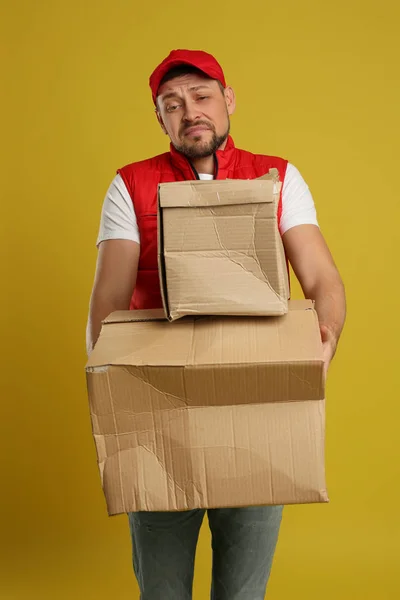 Эмоциональный курьер с поврежденными картонными коробками на желтом бэкгро — стоковое фото