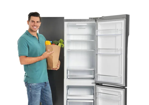 Человек Пакетом Продуктов Рядом Открытым Пустым Холодильником Белом Фоне — стоковое фото