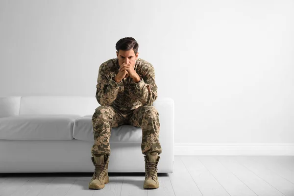 Stressed military officer sitting on sofa near white wall indoor — ストック写真