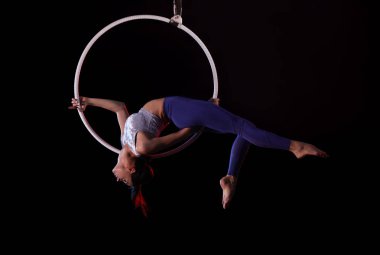 Genç bir kadın içerideki hava halkalarında akrobatik hareketler sergiliyor.