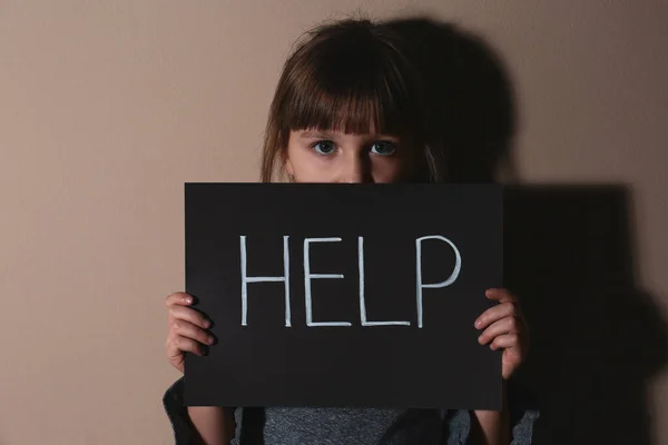 Niña maltratada con signo AYUDA cerca de la pared beige. Viol doméstico — Foto de Stock