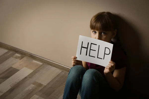 Niña triste con signo AYUDA sentado en el suelo en el interior, espacio f — Foto de Stock