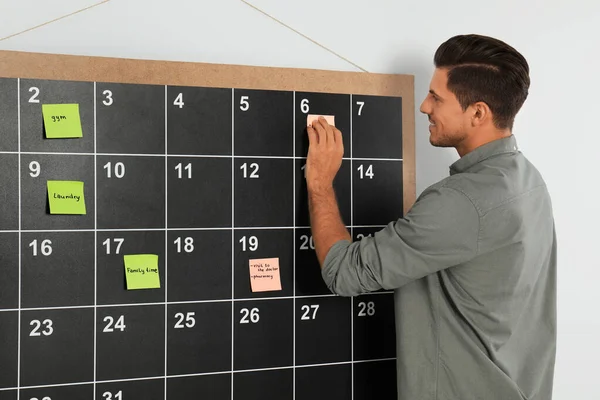 Snygg man sätta klibbig anteckning på ombord kalender — Stockfoto