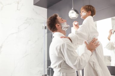 Baba ve oğul yüzlerinde tıraş köpüğü ile banyoda eğleniyorlar.