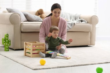 Young nanny and cute little baby playing with toys at home clipart