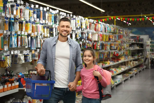 Little girl with father choosing school stationery in supermarket