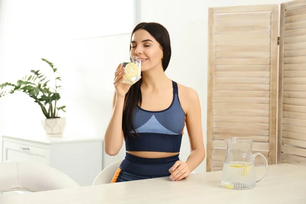 Hermosa joven bebiendo agua de limón en la mesa en el interior —  Fotos de Stock