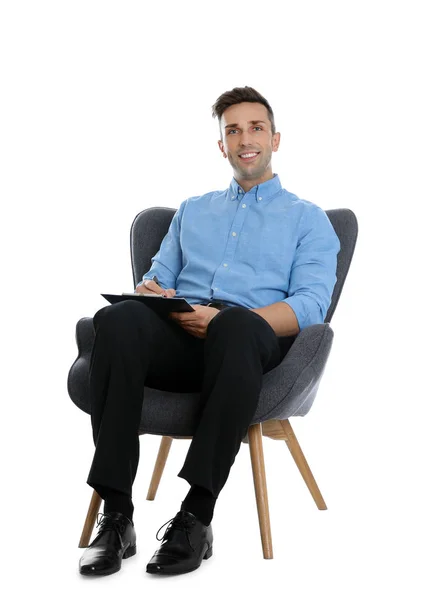 Schöner junger Mann mit Klemmbrett sitzt im Sessel auf weißem B — Stockfoto