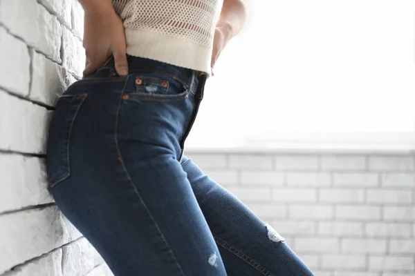 Vrouw met jeans in de buurt van bakstenen muur binnen, close-up — Stockfoto
