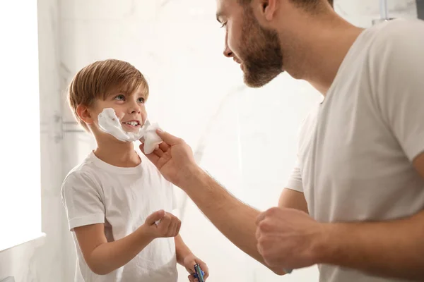 Pai aplicando espuma de barbear no rosto do filho no banheiro — Fotografia de Stock
