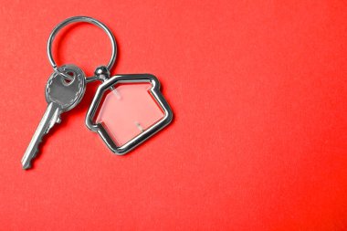 Kırmızı arka planda ev şeklinde ıvır zıvırlı anahtar, üst görünüm ve metin için boşluk. Emlakçılık hizmetleri