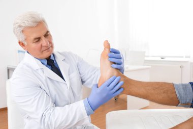 Erkek ortopedist klinikte hastanın ayağını kontrol ediyor.