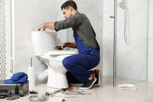 Professional plumber working with toilet bowl in bathroom — 스톡 사진