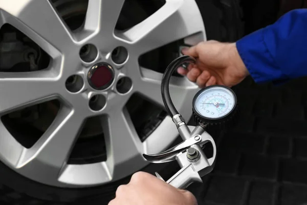 Mechanic checking tire air pressure at car service, closeup