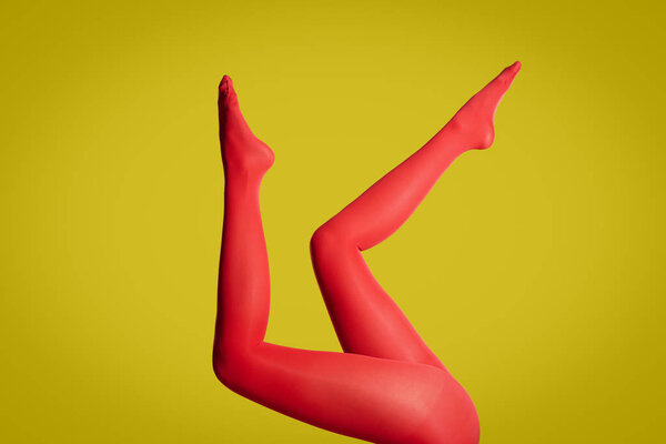 Woman wearing red tights on yellow background, closeup of legs