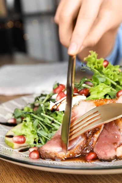 Woman eating delicious salad with roasted duck breast at wooden table, closeup