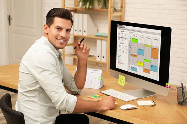 Bonito homem usando aplicativo calendário no computador no escritório — Fotografia de Stock