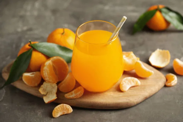 Свежие мандарины и стакан сока на сером столе — стоковое фото