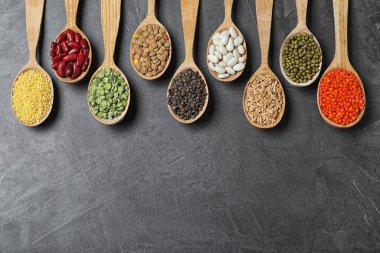 Düz kompozisyon, farklı türde baklagiller ve tahıllar ile koyu gri masa üzerinde, metin için boşluk. Organik taneler