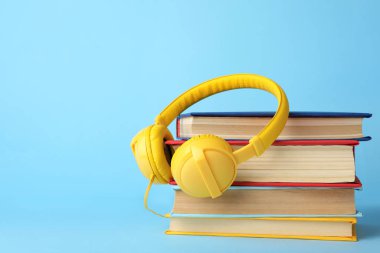 Açık mavi arka planda kitaplar ve modern kulaklıklar. Metin için boşluk