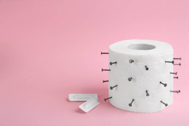 Pembe arka planda çivi ve fitillerle tuvalet kağıdı rulosu, mesaj için yer. Hemoroit sorunları