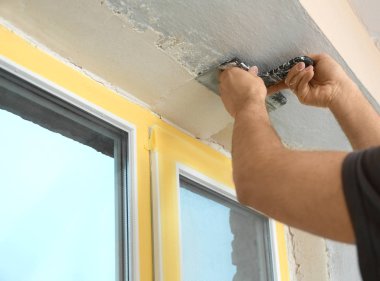 Pencere kenarına macun bıçağıyla sıva yapan bir adam, yakın plan. İç onarım