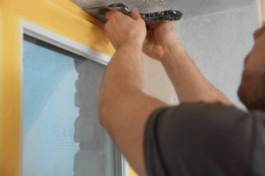 Pencere kenarına macun bıçağıyla sıva yapan bir adam, yakın plan. İç onarım