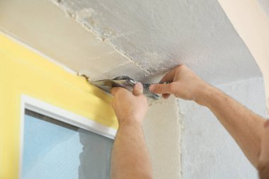Pencere kenarına macun bıçağıyla sıva yapan bir adam, yakın plan. İç onarım